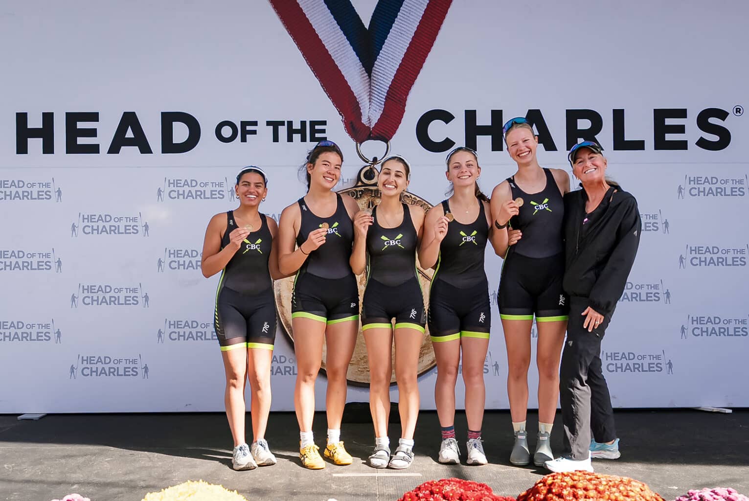 CBC varsity four and coxswain with Coach Liz Trond on the Head of the Charles medal podium, October 2026